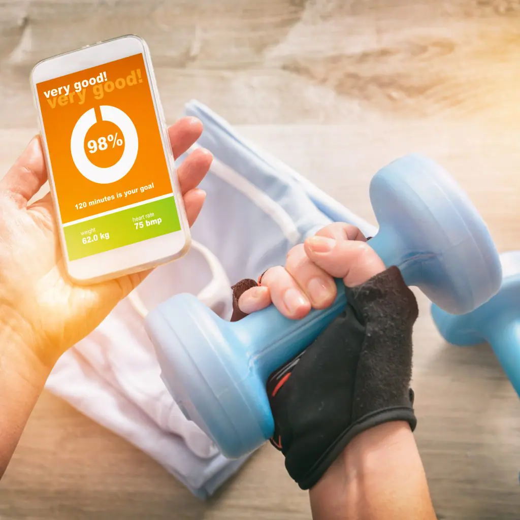 imagem das mãos de uma pessoa, onde uma segura o celular com o aplicativo aberto e a outra segura um pesinho de musculação